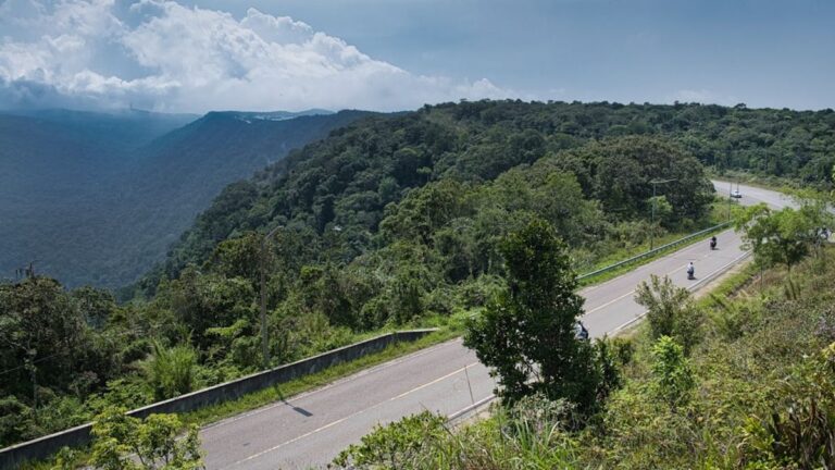 Ciclista de mountain bike em trilha desafiadora na Serra do Espinhaço, Brasil, com montanhas e vegetação ao fundo.